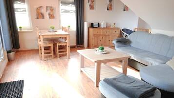 Ein Wohnzimmer mit Holzboden, einer Couch, einem Couchtisch, einem Esstisch mit Stühlen und einem Schrank.