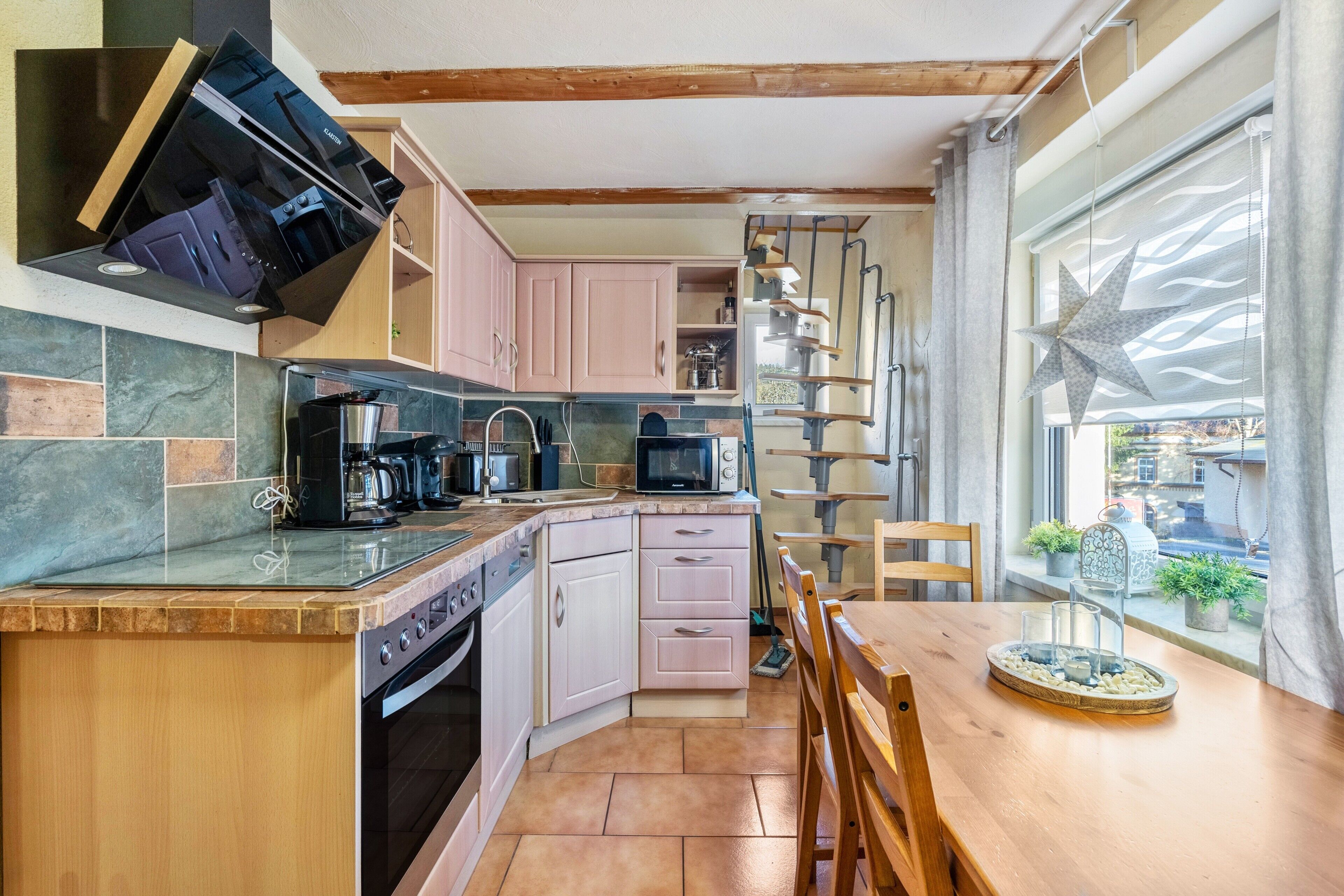 Une cuisine équipée d’une cuisinière intégrée, d’un four à micro-ondes et d’une machine à café, une table à manger en bois avec des chaises, et une grande fenêtre décorée d’une étoile.