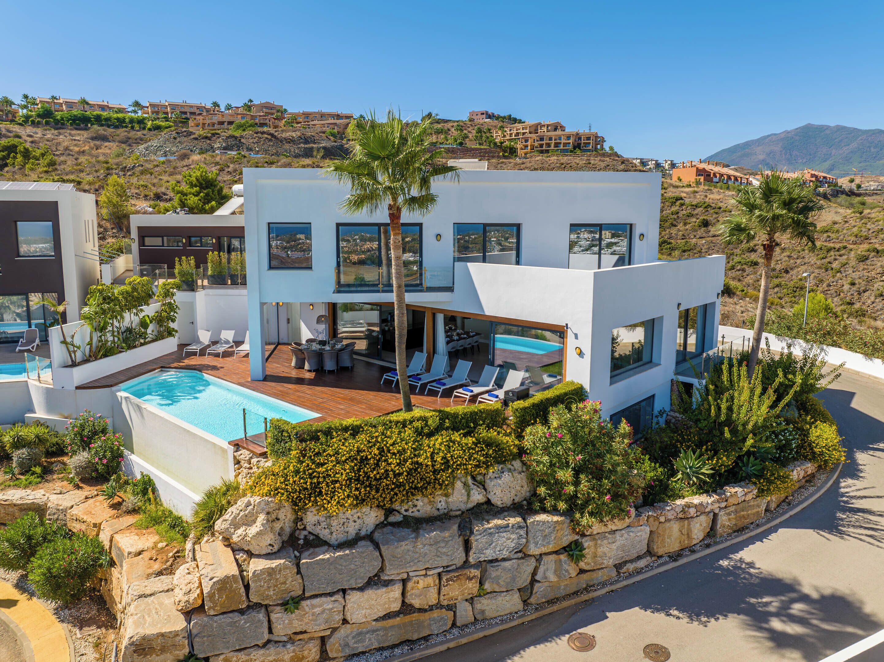 A modern two-story house with a swimming pool, outdoor seating, and a view of the surrounding landscape.