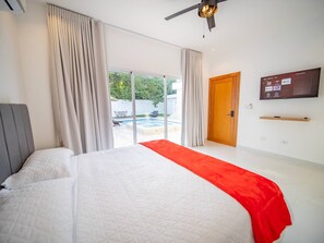 Une chambre d’hôtel moderne dotée d’un grand lit, d’un ventilateur de plafond, d’une télévision et d’une porte-fenêtre coulissante donnant sur un espace piscine.