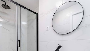 Une salle de bain moderne avec une douche à parois de verre, un lavabo blanc avec une serviette et un miroir rond accroché au mur.