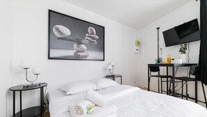 Une chambre d’hôtel avec un lit soigneusement fait, un bureau avec une chaise, un téléviseur à écran plat fixé au mur et un tableau encadré au-dessus du lit.