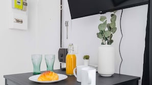 Une pièce moderne avec une table en bois foncé, deux chaises noires, un téléviseur à écran plat fixé au mur, une petite plante en pot et un vase blanc.