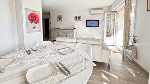 A dining area with a table set for four, a sofa, a TV, and a view of the outside.