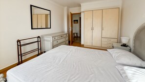 A bedroom with a bed, dresser, wardrobe, bedside table, lamp, and a mirror.