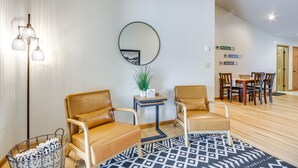 Un salon moderne avec des fauteuils en cuir, un miroir rond, une petite table ornée d’une plante, et un coin repas à l’arrière-plan.