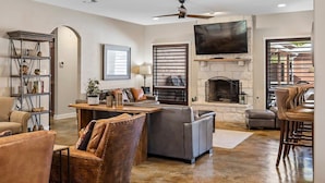 A spacious living room with a fireplace, a television mounted on the wall, and a ceiling fan. - 4BR: Hot tub, Pool/ Fireplaces/ Grill/ Family Fun (Fredericksburg)