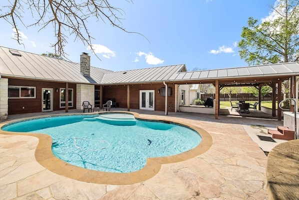 A swimming pool with a stone deck, a covered patio, and a stone chimney.