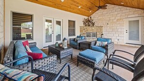 An outdoor patio with wicker furniture, a stone fireplace, and a ceiling fan. - 4BR: Hot tub, Pool/ Fireplaces/ Grill/ Family Fun (Fredericksburg)
