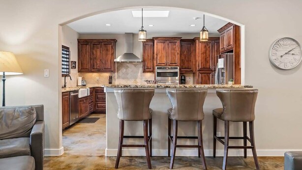 A kitchen with wooden cabinets, a central island with bar stools, and a clock on the wall. - 4BR: Hot tub, Pool/ Fireplaces/ Grill/ Family Fun (Fredericksburg)