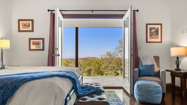 Ein Schlafzimmer mit Bett, einer Bank, einem Stuhl, einem Tisch und Blick ins Freie.
