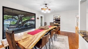 Ein Essbereich mit einem Holztisch, Stühlen und Blick auf einen Grillbereich durch große Fenster.