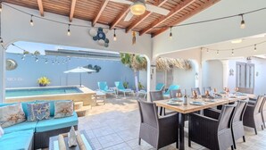 Une terrasse extérieure avec une piscine, des chaises longues et un coin repas aménagé avec des meubles en osier.