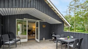 Eine Terrasse im Freien mit Tisch und Stühlen, einem Grill und einer Glasglastür, die zu einem Innenbereich führt.