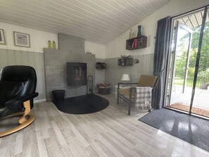 Ein gemütliches Wohnzimmer mit Kamin, einem schwarzen Ledersessel, einem Esstisch mit Stühlen und Blick ins Freie durch eine Glastür.