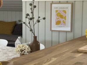 A dining area with a wooden table, a vase with white flowers, and a framed artwork on the wall.