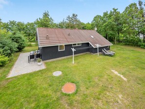 Ein eingeschossiges Haus mit Ziegeldach, einer Terrasse mit Gartenmöbeln und einem kleinen Garten.