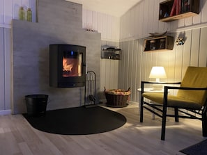 A cozy living room with a fireplace, a comfortable chair, a lamp, and a bookshelf.