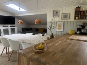 A modern kitchen with a wooden countertop, white chairs, and pendant lights.