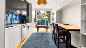 Een moderne keuken met witte kasten, een inbouwoven en een groot raam met uitzicht op een achtertuin.