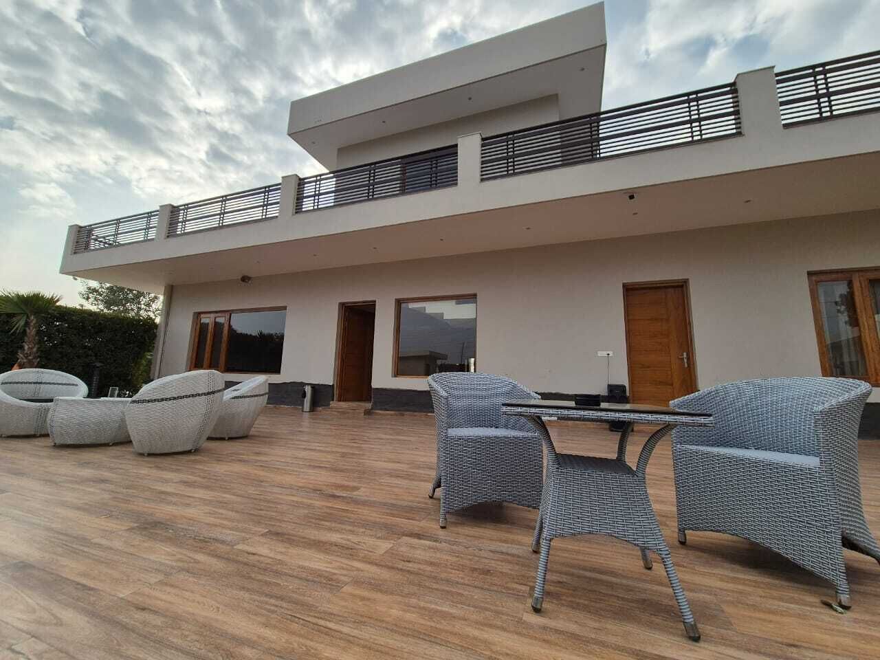 A modern two-story house with a patio area featuring wicker furniture and a wooden deck.