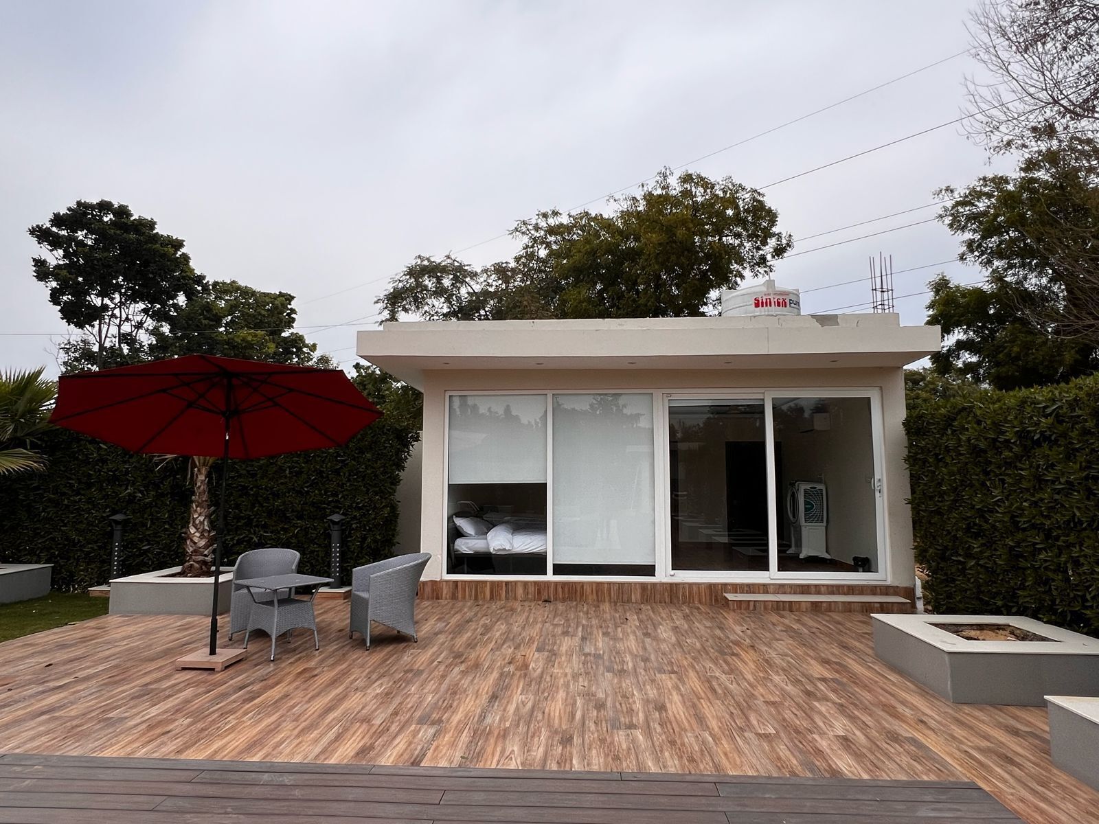 Una casa moderna con terraza de madera, un paraguas rojo y un ventanal de vidrio que da a un dormitorio.