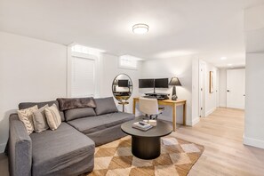 A modern living room with a grey sectional sofa, a round coffee table, a TV, and a desk with a computer. - Upscale 5BR/3BA w/ Jacuzzi (Oak Park)