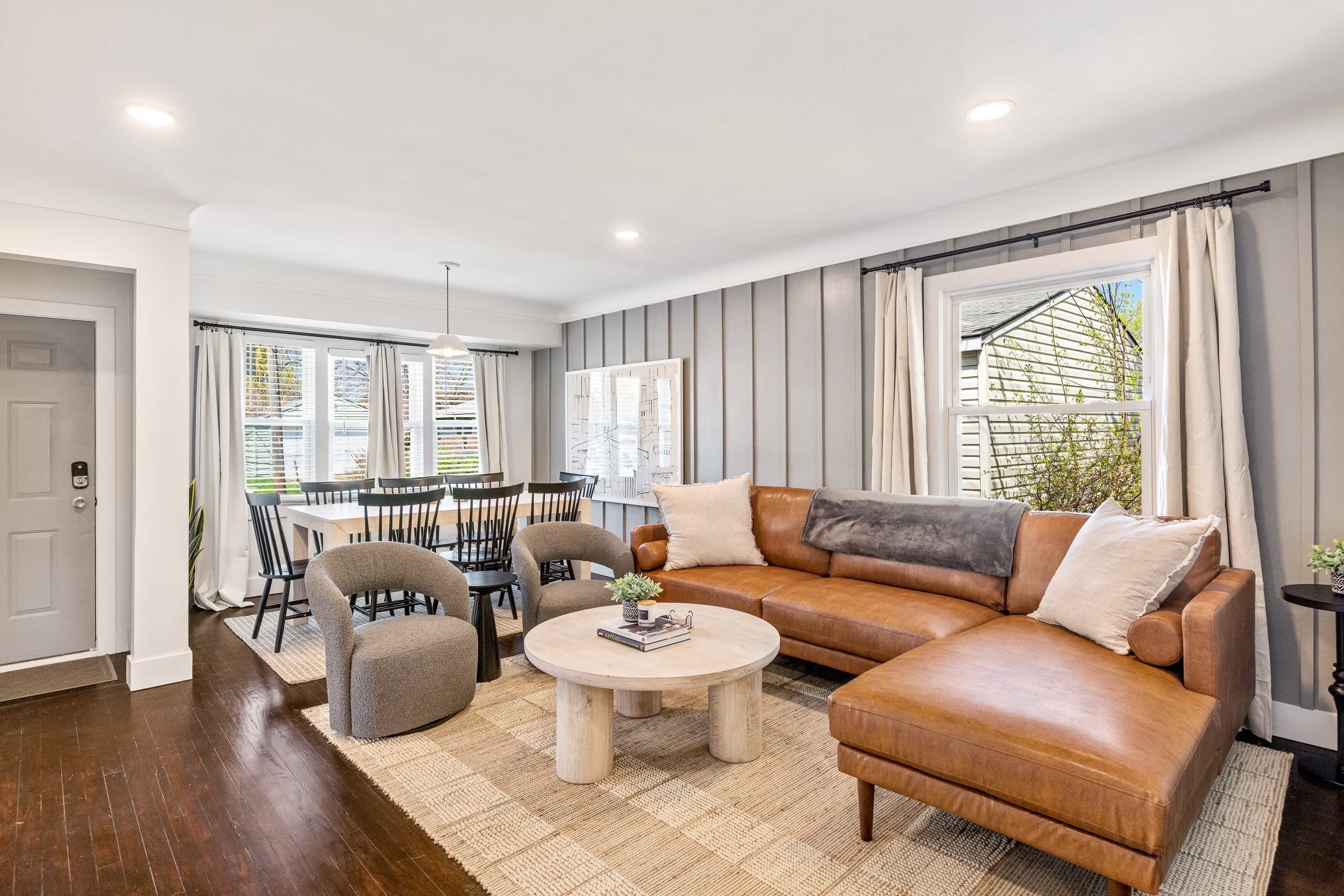 A modern living room with a leather sofa, a round coffee table, and a dining area with chairs and a table.