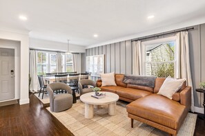 A modern living room with a leather sofa, a round coffee table, and a dining area with chairs and a table. - Upscale 5BR/3BA w/ Jacuzzi (Oak Park)