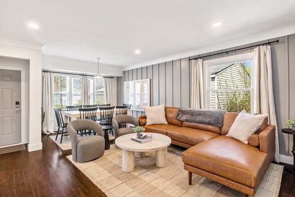 A modern living room with a leather sofa, a round coffee table, and a dining area with chairs and a table.