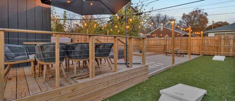 A wooden deck with outdoor furniture, a covered area with an umbrella, and a grassy yard.