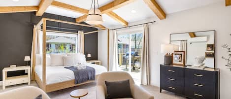 Un dormitorio moderno con cama con dosel, un aparador oscuro, una silla y un ventanal grande.