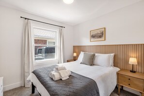 A hotel room with a bed, a window with curtains, a bedside table with a lamp, and a framed picture on the wall.