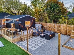 A backyard with a wooden deck, outdoor furniture, and a string of lights.