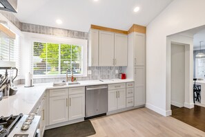 A modern kitchen with white cabinets, a dishwasher, a stove, and a window with blinds.