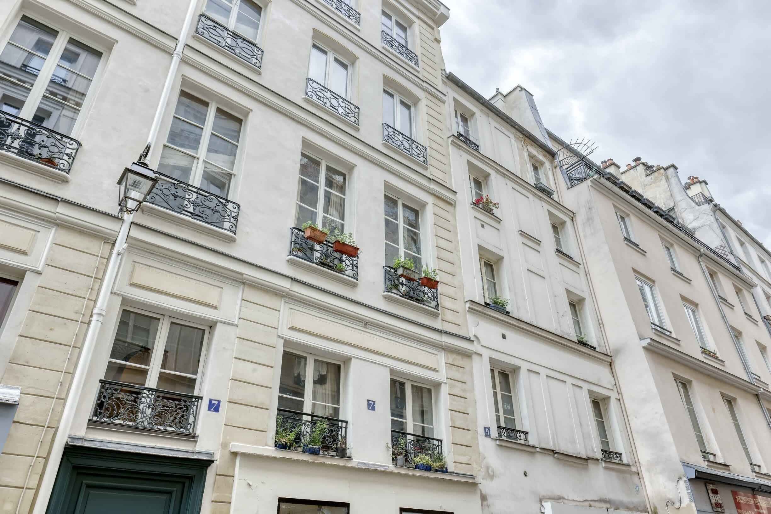 A multi-story building with balconies, each with wrought iron railings and potted plants.