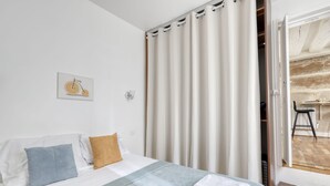 Ett hotellrum med en säng, kuddar, en tavla, ett fönster med gardiner och utsikt över en matsal.
