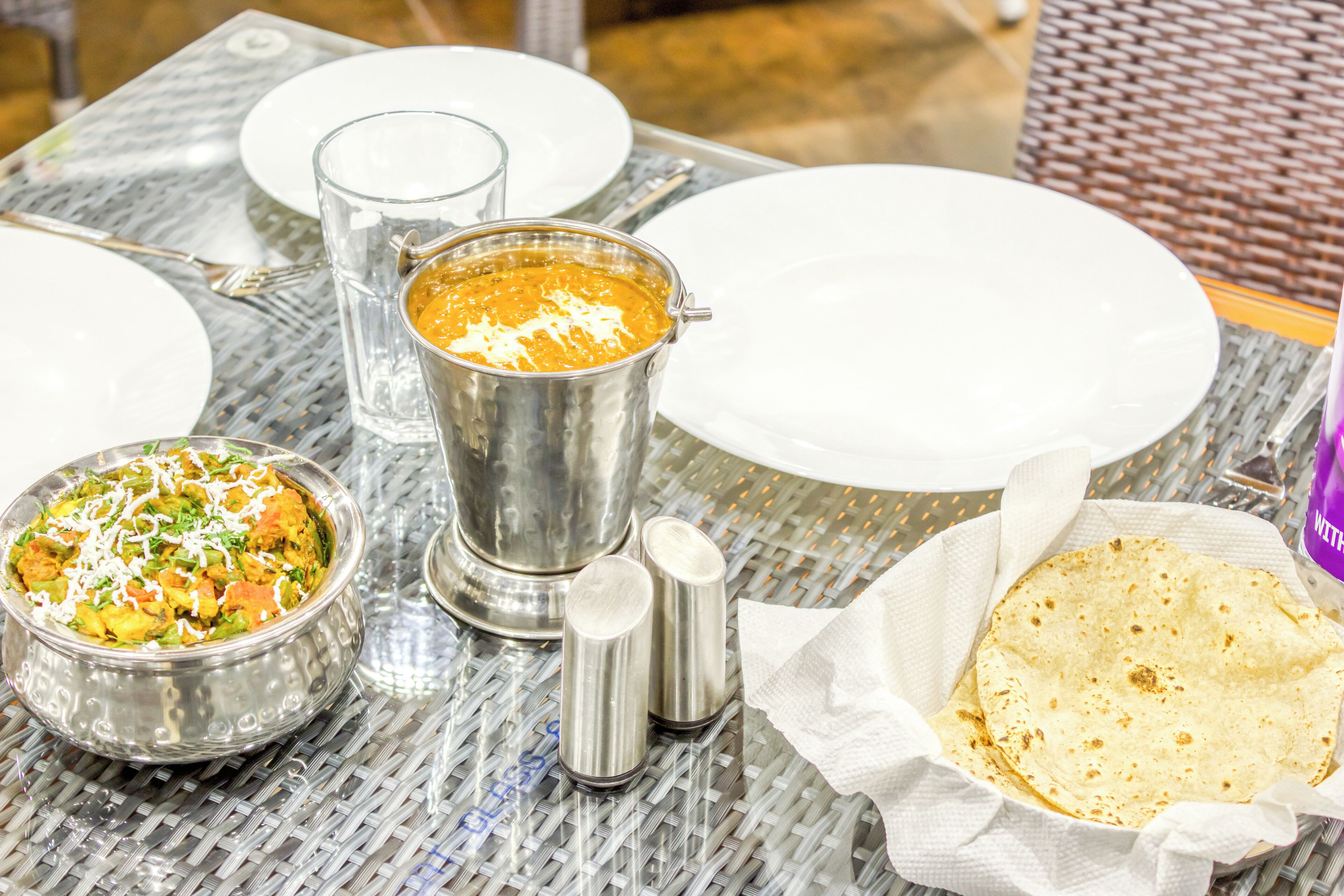 A table set with a metal pitcher, a bowl of food, salt and pepper shakers, a glass, and a plate.