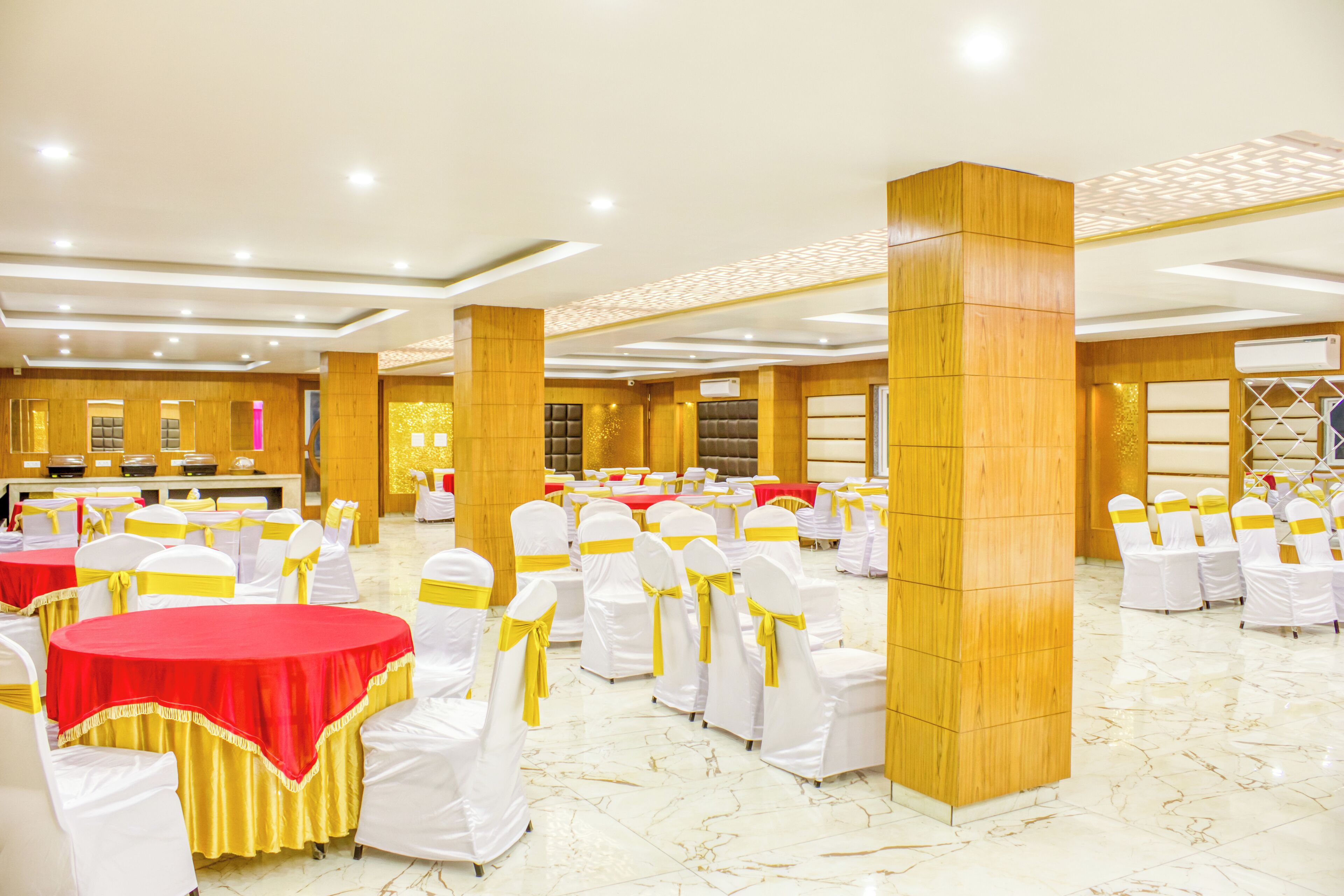 A banquet hall with round tables, white chairs with yellow sashes, and a polished marble floor.