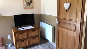 A room with a television on a wooden TV stand, a radiator, a wooden door with a heart-shaped decoration, and two wall-mounted chicken-themed artworks. - Albertine's bed and breakfast near Sancerre Guédelon and St Fargeau (LERE)