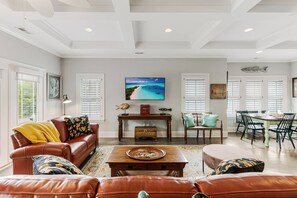 Una sala de estar amplia con un televisor grande, una mesa de centro de madera y un comedor con sillas y una mesa.