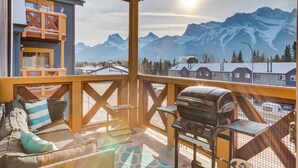 A balcony with a grill, seating, and a view of snow-capped mountains.
