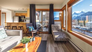 A modern living room with a sofa, a coffee table with a plant, and a view of mountains through large windows.