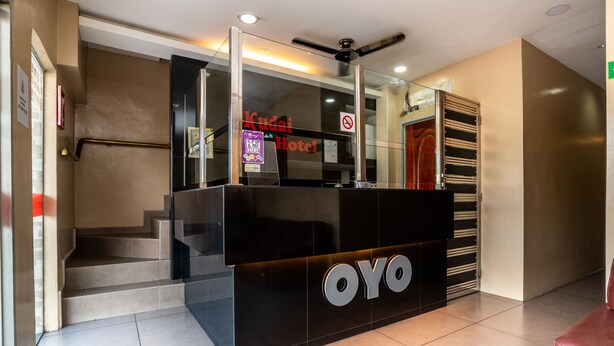 Un mostrador de recepción con separador de vidrio, un letrero de “No Fumar” y un letrero del “Kuda Hotel”.