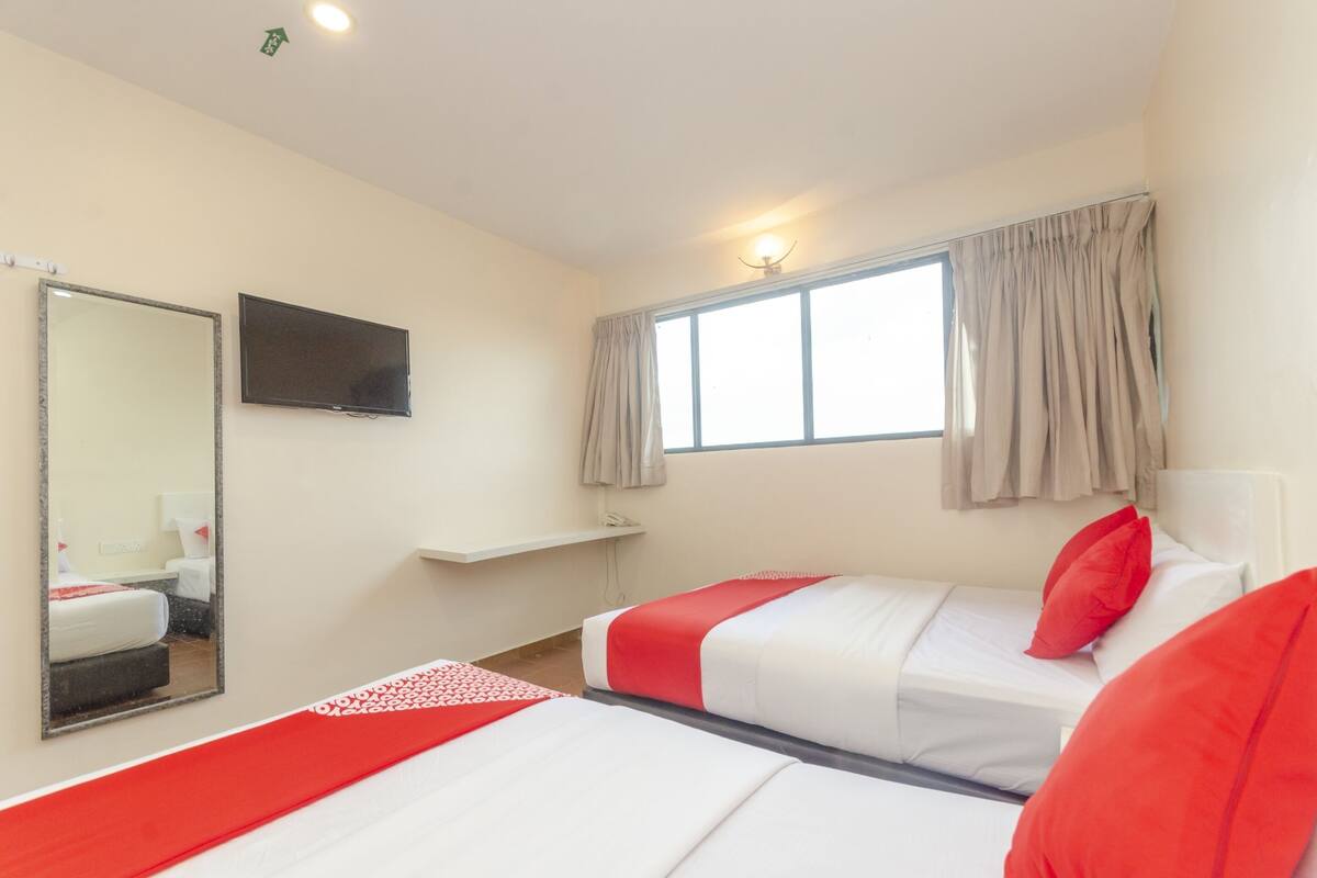 Habitación de hotel con dos camas, un televisor, una ventana con cortinas y un espejo.