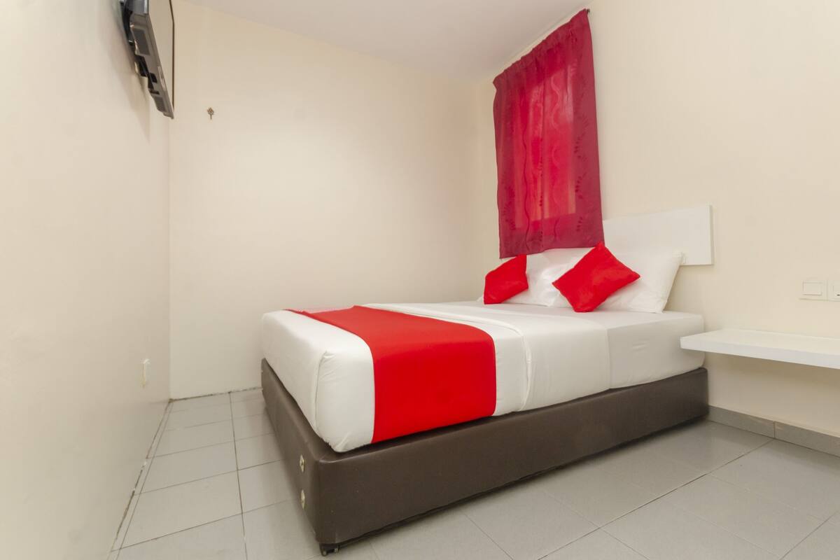 Un dormitorio moderno con cama, ropa de cama roja y blanca, una cortina roja y una mesita de noche blanca.