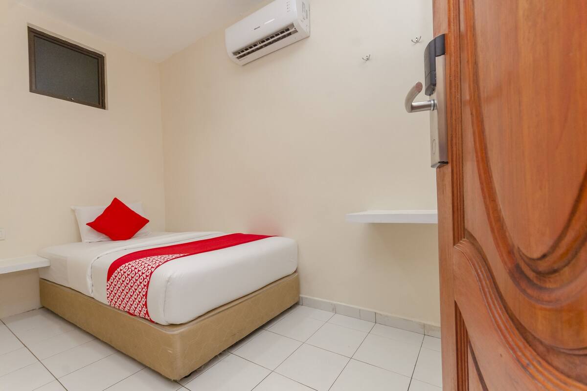 Habitación de hotel con cama, mesita de noche, puerta de madera y unidad de aire acondicionado en la pared.