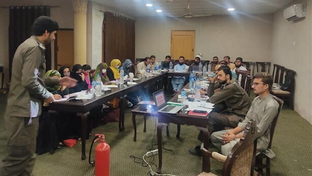 A conference room with a long table, chairs, and attendees. - M M Palace Guest House Peshawar (Peshawar)