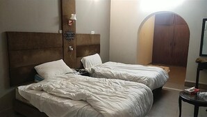 A hotel room with two beds, a wooden headboard, a nightstand, and a small table. - M M Palace Guest House Peshawar (Peshawar)