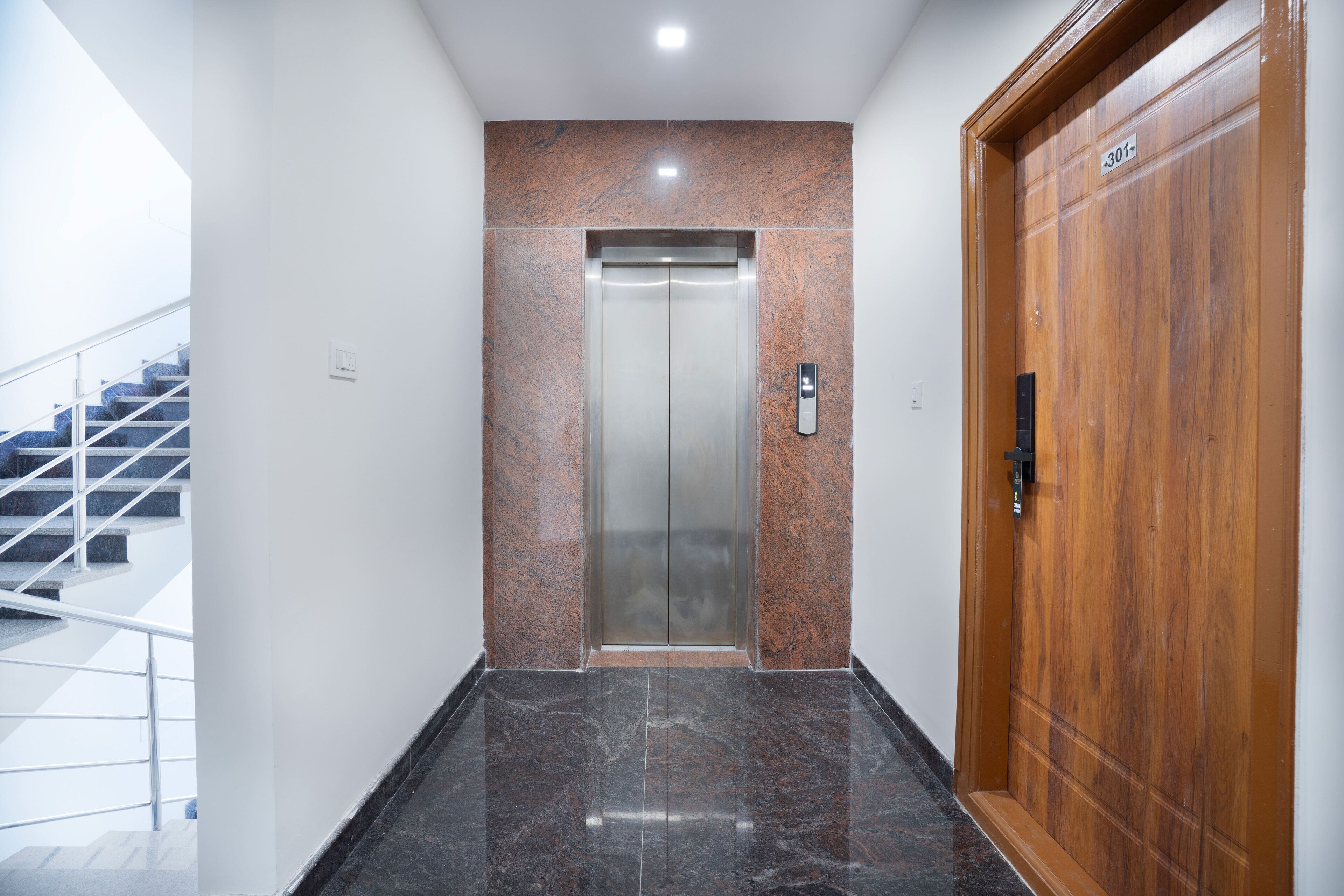 A modern elevator with a marble wall and a wooden door, leading to a staircase.